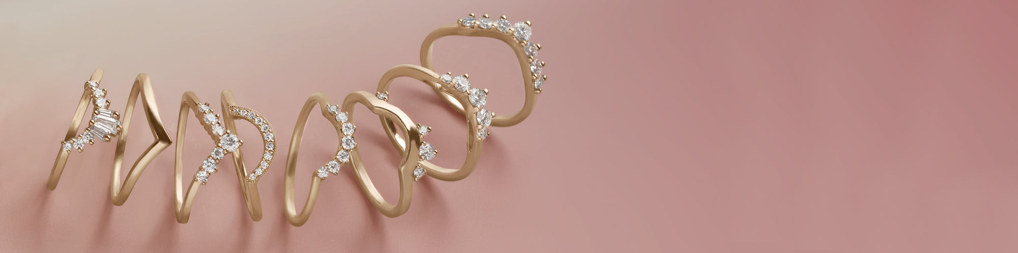 A cascade of white diamond bands set in yellow gold in different silhouettes on a pink background.