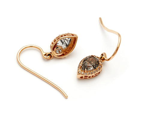 A pair of 14k yellow gold drop earrings featuring pear shaped black rutile quartz encircled in a champagne diamond halo against a white background.