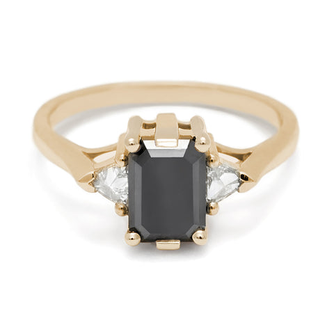 A three stone engagement ring with an emerald cut and emerald shape 7x5mm black diamond center stone with two white diamond trillion side stones set in yellow gold., Yellow Gold