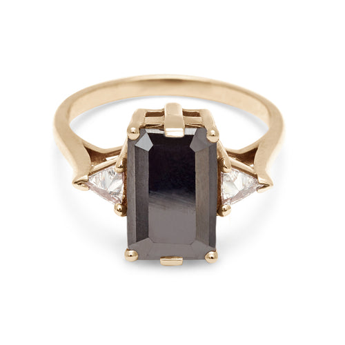 A three stone engagement ring with an emerald shape black diamond center stone with two white diamond trillion side stones set in yellow gold., Yellow Gold