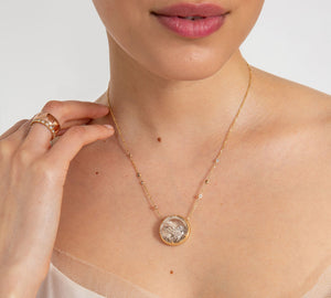 A lighter-complexion model gracefully touches her shoulder wearing two stacked wedding bands, one with white diamonds. On her neck she wears a cabochon necklace made with quartz and mixed diamonds.