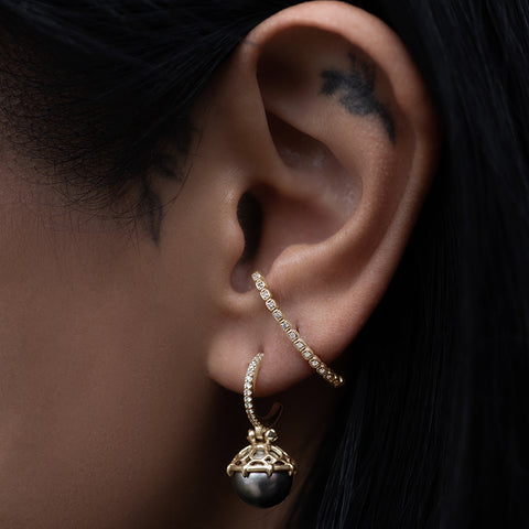 A single hoop with a light pearl hanging from it with grey diamond accents on either side set in yellow gold on a medium-complexion ear with a white diamond ear climber next to it., White Gold, Rose Gold, Yellow Gold 2