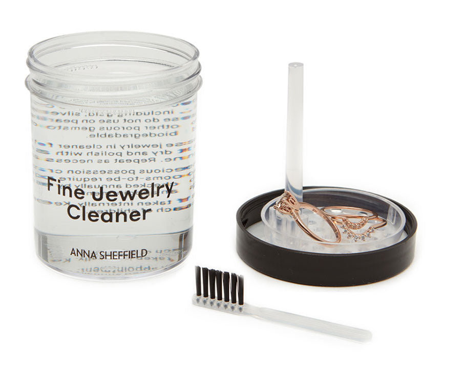 To the left of the image is a fine jewelry cleaner. On the right is a brush and rings in the cleaner top.