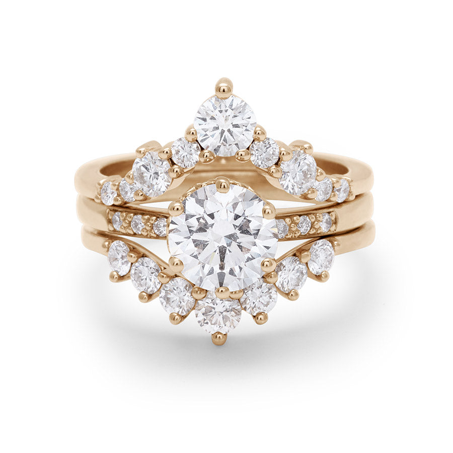 A solitaire round white diamond engagement ring stacked between a chevron bands and a curve band with white diamonds.