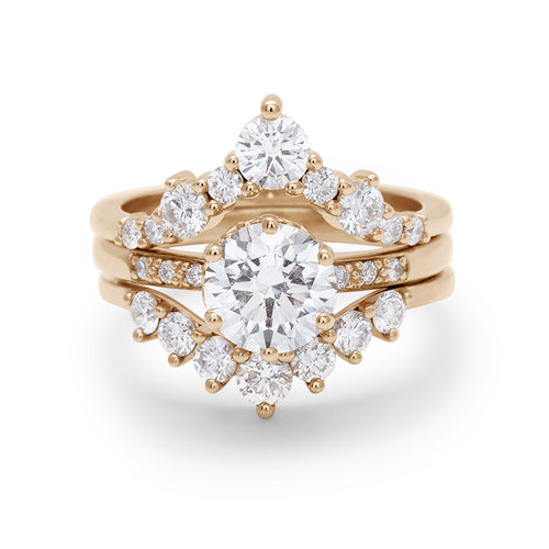 A solitaire round white diamond engagement ring stacked between a chevron bands and a curve band with white diamonds.