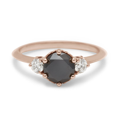 A three stone engagement ring with a round shape black diamond center stone with two white diamond round side stones set in rose gold., Rose Gold