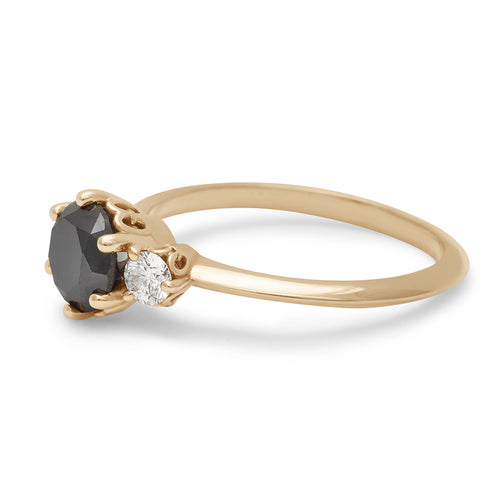 Angled view of a three stone engagement ring with a round shape black diamond center stone with two white diamond round side stones set in yellow gold., Yellow Gold