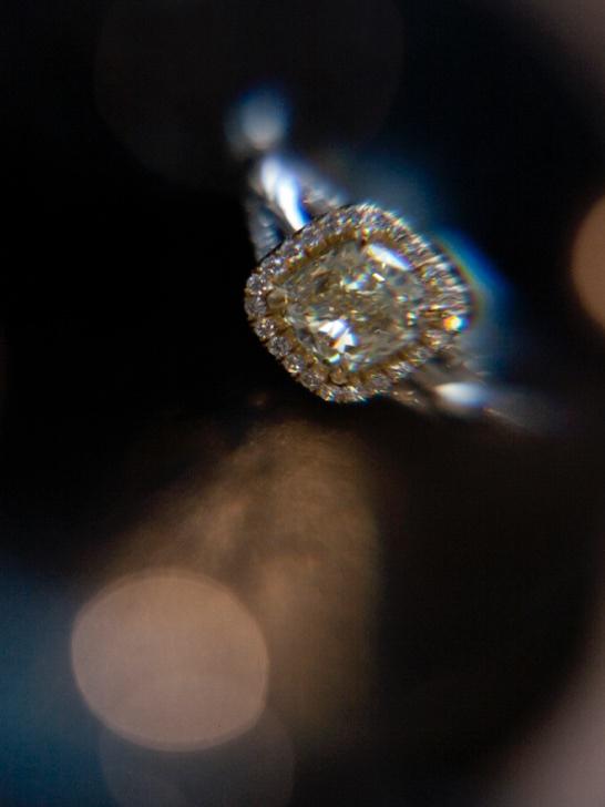 A close up of a yellow diamond engagement ring with a halo and white gold shank with a soft focus that appears as if the ring is floating in outer space.