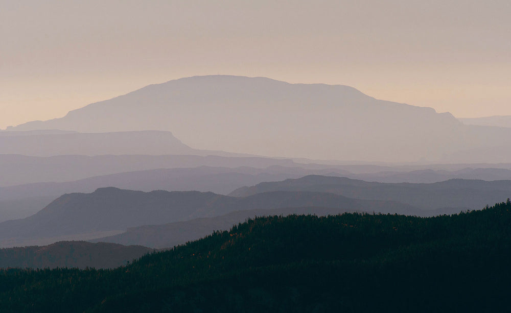 A photo of a mountain plane from a distance, with the varying distanced graduating in color from soft pinks to dark purples.