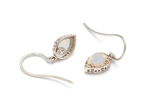 A pair of sterling silver drop earrings featuring pear shaped rainbow moonstones encircled in a champagne diamond halo against a white background.