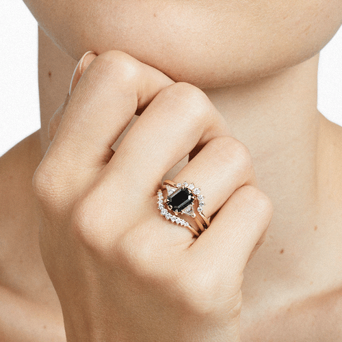 A three stone engagement ring with a black diamond center stone stacked between two white diamond nesting bands on a light-complexion model's hand., White Gold, Rose Gold, Yellow Gold
