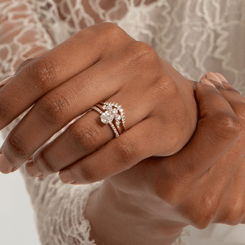 An oval engagement ring with pave on the band stacked beneath two curve nesting bands on a dark-complexion model's left ring finger., White Gold, Rose Gold, Yellow Gold