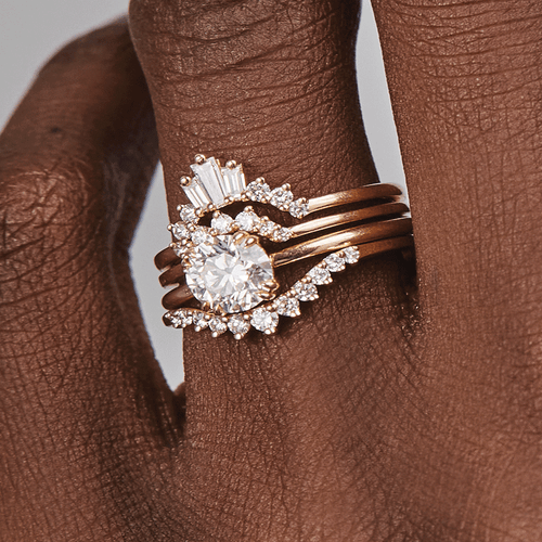 A solitaire white diamond engagement ring stacked between three white diamond nesting bands on a dark-complexion model's hand., White Gold, Rose Gold, Yellow Gold
