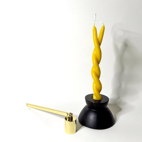 A black candle holder holding a yellow twisted candle to symbolize a twin flame with a brass candle snuffer next to it.