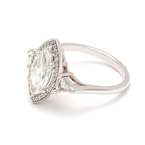 Angled view of a three stone engagement ring with a marquise shape 1.50ct white diamond center stone surrounded by a white diamond pave halo with two white diamond trillion side stones set in platinum. 6