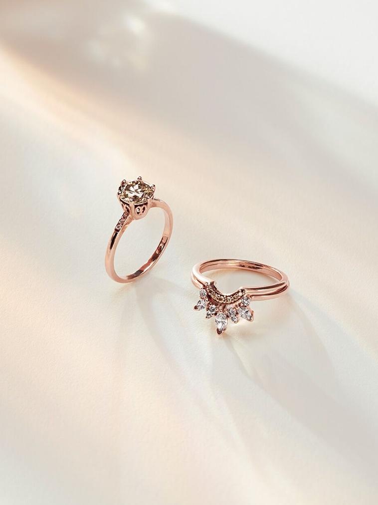 An image of the Hazeline Solitaire Engagement ring with a champagne diamond center, propped upwards towards the sky so the basket of the ring can be seen. Beside the engagement ring is a set of nesting bands with white diamonds.