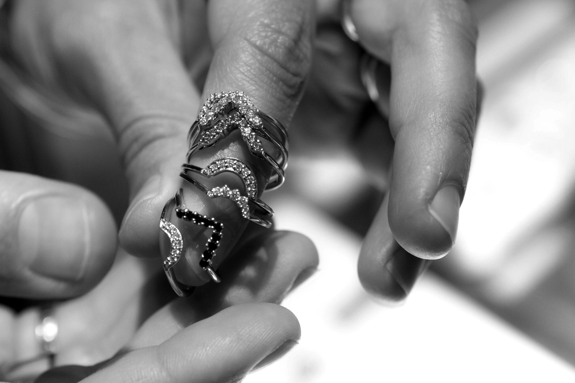 A black and white close up image of a hand with seven wedding bands graduating along the finger from tip to knuckle.