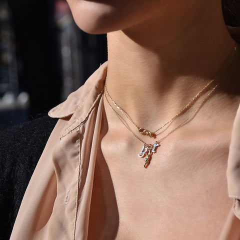 A medium sized serpent pendant set in yellow gold on a yellow gold chain with two gothic initial charms next to it with a serpent choker necklace above on a medium-complexion model's neck. 2
