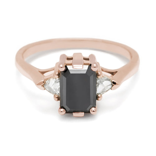 A three stone engagement ring with an emerald cut and emerald shape 7x5mm black diamond center stone with two white diamond trillion side stones set in rose gold., Rose Gold