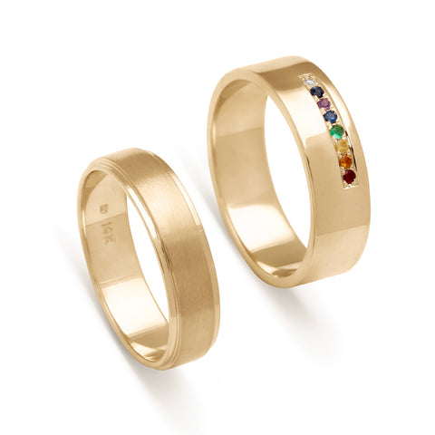 A 5mm flat edge band with a brushed finished set in yellow gold next to a 6mm flat band with a line of rainbow gemstone set in yellow gold.