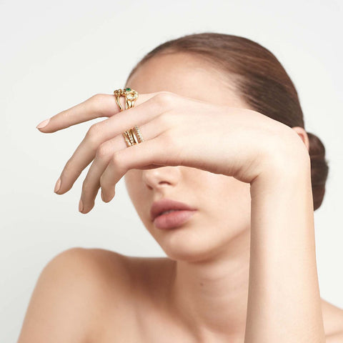 A serpent band with a green emerald center stone and white diamond accent stones around the head of the snake set in yellow gold on a lighter-complextion hand paired with another serpent band. 5