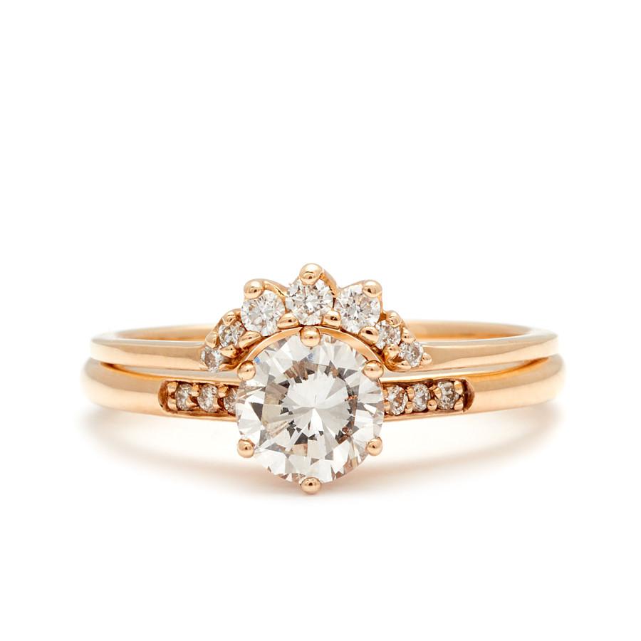 A solitaire ring with a round white diamond with white diamond pave on either side set in yellow gold below a 7 white diamond tiny curve band.