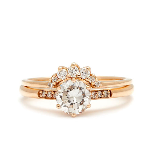 A solitaire ring with a round white diamond with white diamond pave on either side set in yellow gold below a 7 white diamond tiny curve band.