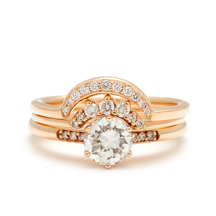 A solitaire ring with a round white diamond with white diamond pave on either side set in yellow gold below a 7 white diamond tiny curve band and a crescent shaped white diamond band.