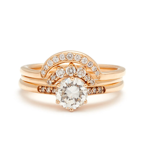 A solitaire ring with a round white diamond with white diamond pave on either side set in yellow gold below a 7 white diamond tiny curve band and a crescent shaped white diamond band.