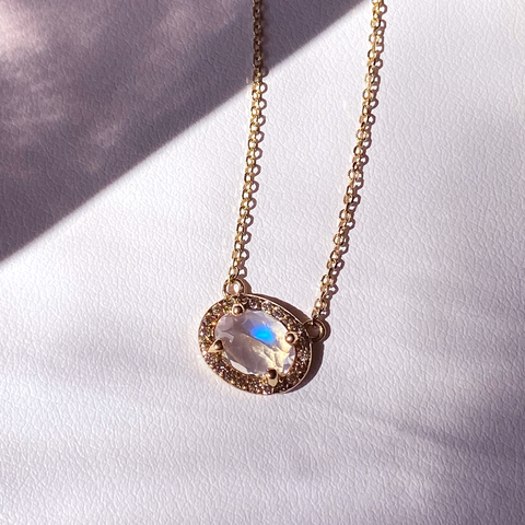 A necklace with an oval shape rainbow moonstone center stone surrounded by a champagne diamond pave halo set in yellow gold on a yellow gold chain on a grey background., White Gold, Rose Gold, Yellow Gold 4