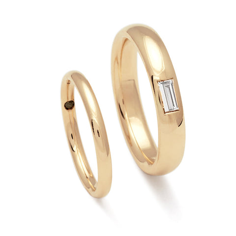 A 2mm classic round band set in yellow gold with a hidden black diamond next to a 4mm classic round band with a white diamond baguette set in yellow gold.