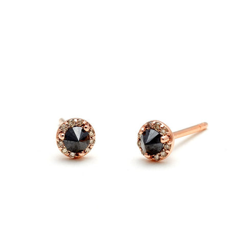 A pair of tiny black diamond center stone earrings with a halo of champagne diamond set in rose gold one earring angled. 2