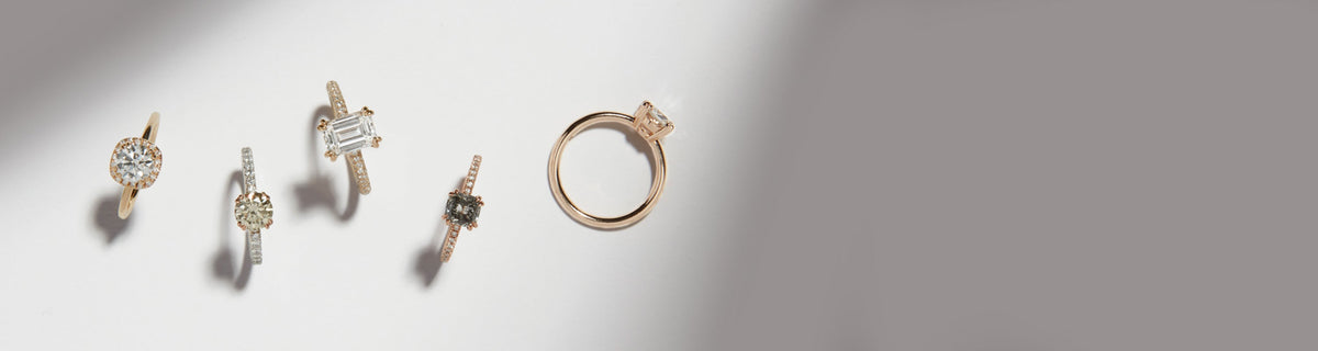 A line of a variety of diamonds and different shaped engagement rings on a grey and white background.