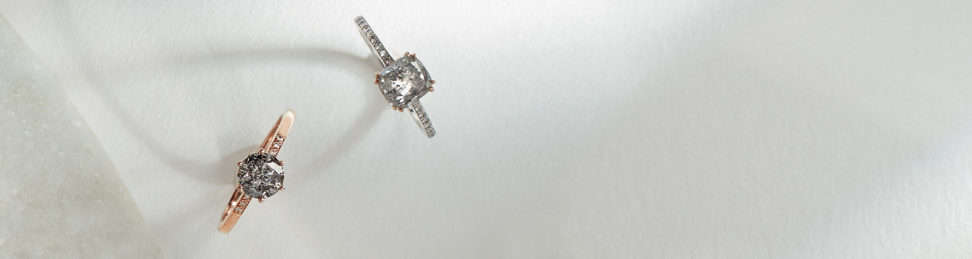Two solitaire grey diamond engagement rings with white diamond pave on the band on a grey background.