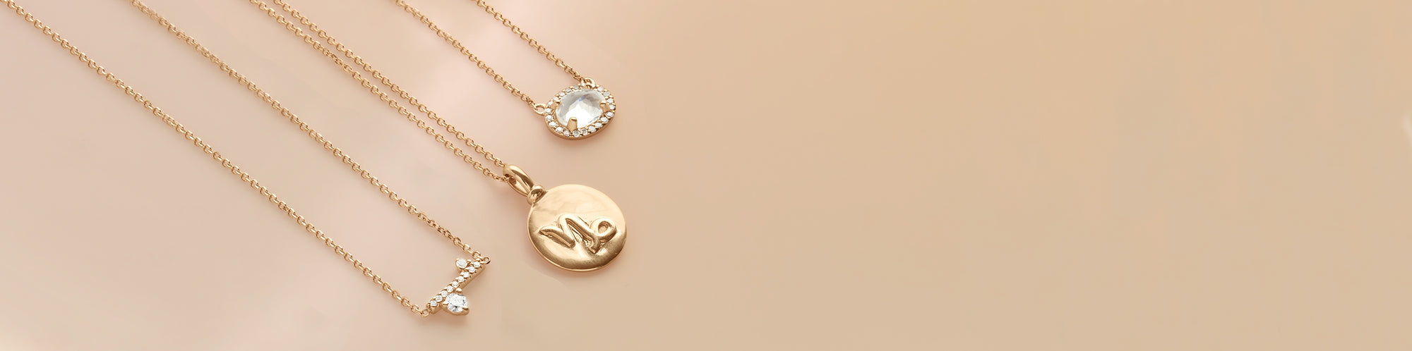 A white diamond necklace, a Capricorn sign necklace, and a rainbow moonstone necklace on a peach colored background.