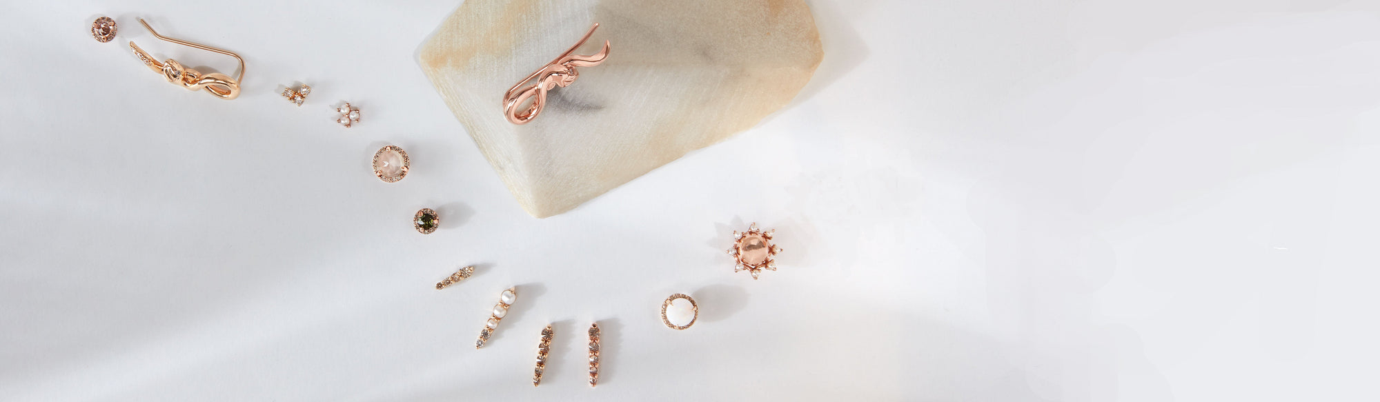 An array of stud earrings curved around a tan stone on a grey background.