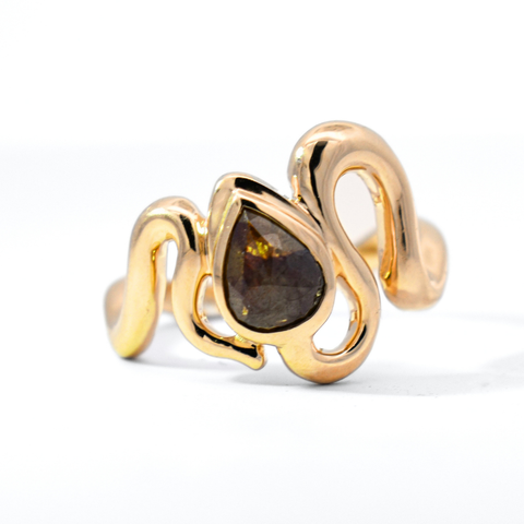 A ring inspired by the organic curving silhouette of a serpent featuring a brown pear cut diamond set in yellow gold against a white background. 