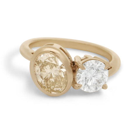 Toi et moi engagement ring featuring an oval champagne diamond and a white round diamond set in yellow gold. 