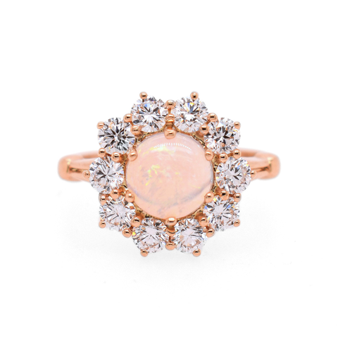 A ring featuring a cabochon fire opal center stone encircled in 3mm white round diamonds to create a flower appearance set in rose gold. 