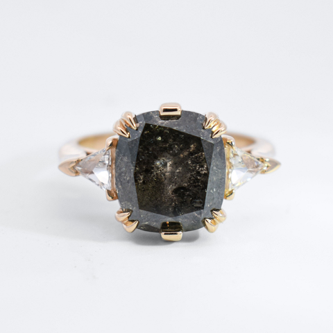 A three stone ring featuring a black oval rose cut diamond and white trillion diamond side stones set in yellow gold. 
