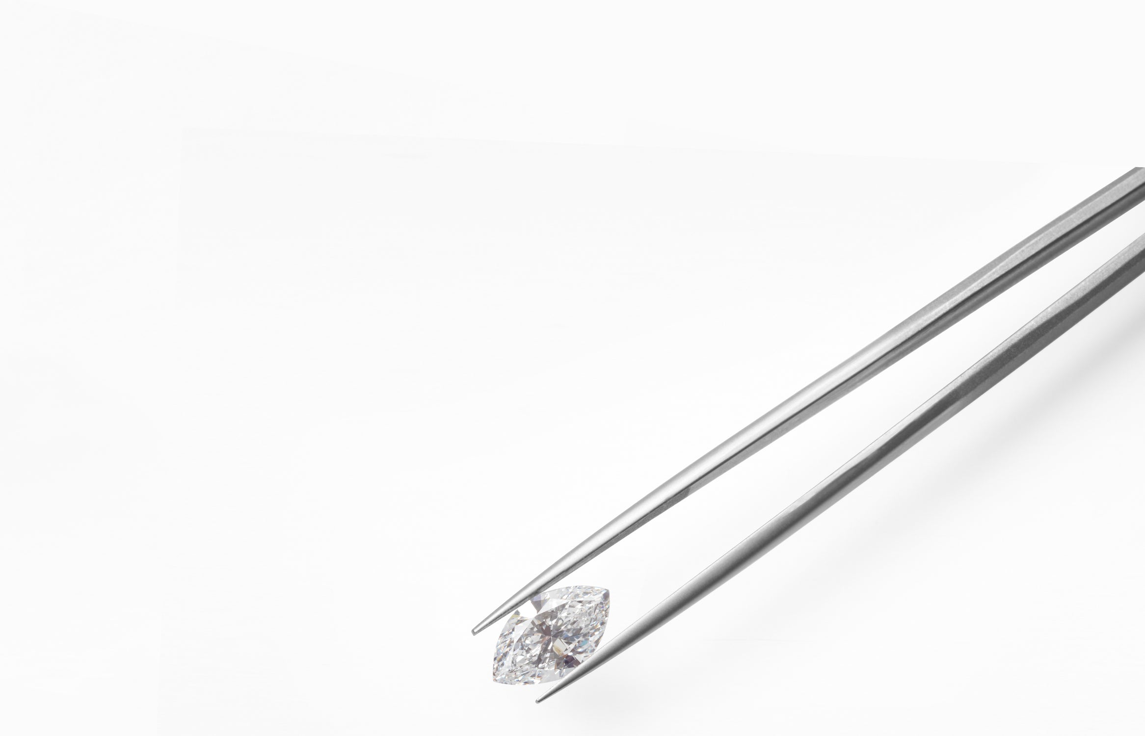 a loose white diamond marquise held by tweezers on a white background