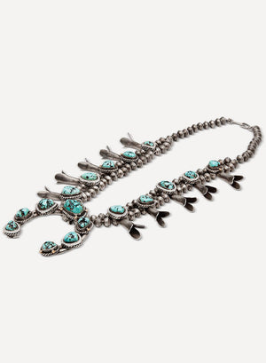 A sterling silver necklace with accents of 14k yellow gold, diamond melee, and turquoise gemstones set on a pink/white background.