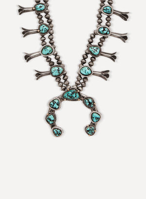 A sterling silver necklace with accents of 14k yellow gold, diamond melee, and turquoise gemstones set on a pink/white background.