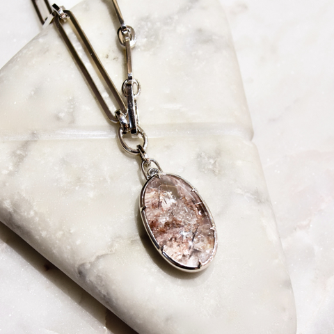 An oval cabochon garden quartz pendant set in white gold on a white gold chain placed on a white marbled stone surface. 