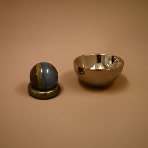 Two decorative items, a spherical jasper gemstone object with a metallic bronze base and a bronze reflective bowl, on a beige background.