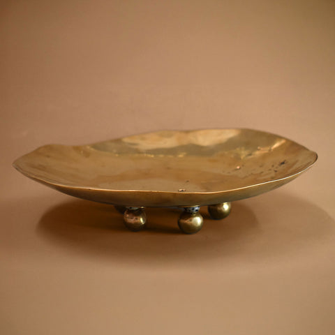 A bronze dish with dalmation jasper sphere and bronze sphere feet on a beige background