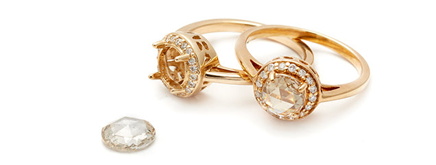 2 halon style engagement rings sit overlapping each other with rose cut diamonds in the center. One of the rings does not have the diamond yet set in the setting.