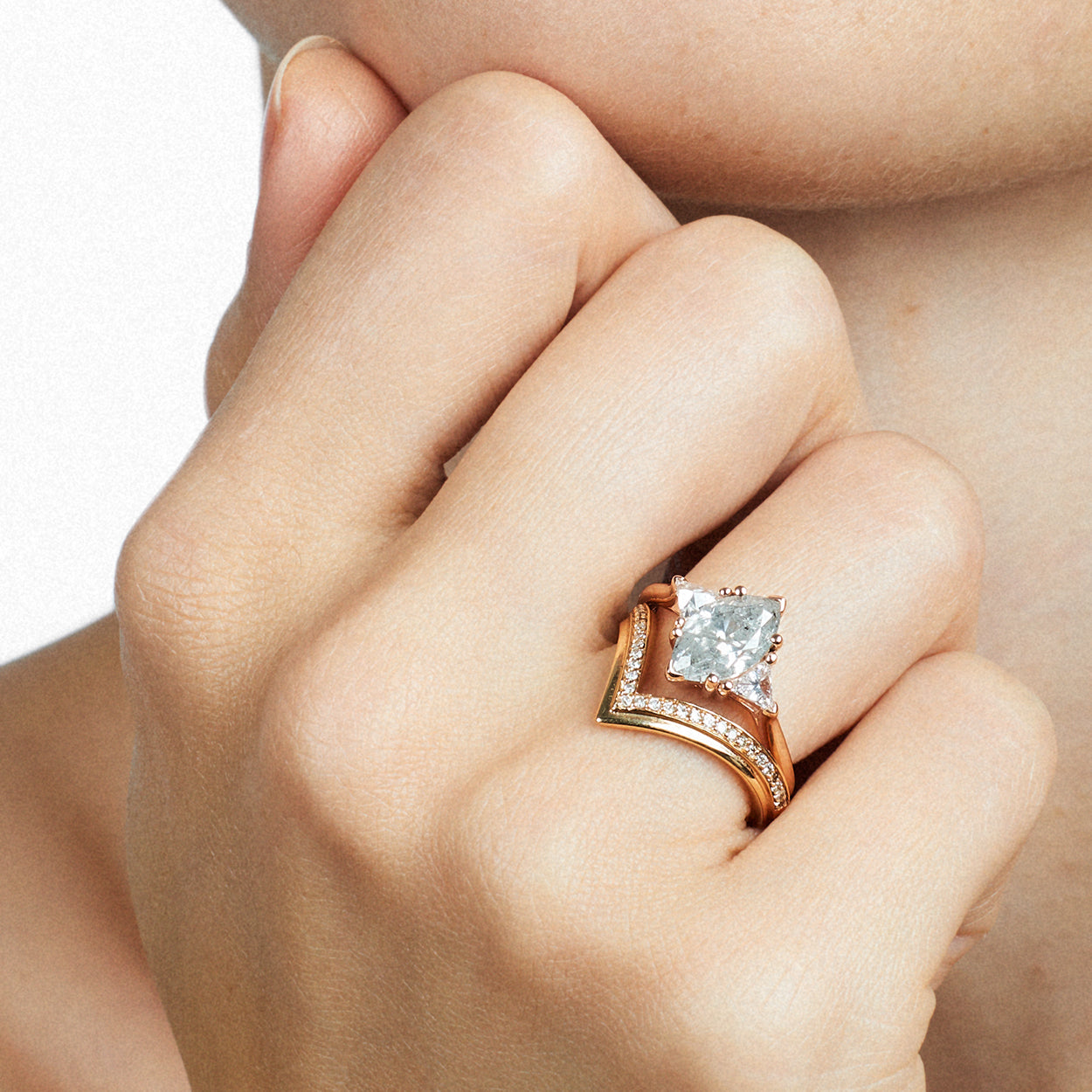 A three stone engagement ring with an marquise shape grey diamond center stone with two white diamond trillion side stones set in yellow gold above a chrysalis band with white diamonds set in yellow gold on a model. Available in White Gold, Yellow Gold, Rose Gold.