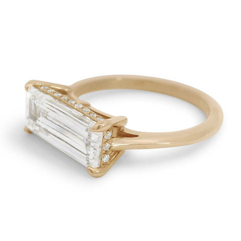 An elongated step cut white diamond set in a yellow gold band with a hidden halo of smaller white diamonds beneath it.