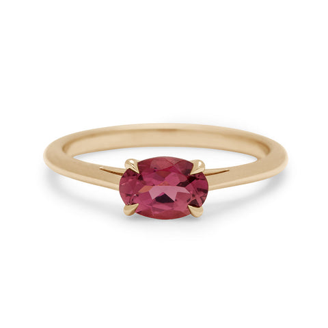 An east/west solitaire ring with an oval pink tourmaline center stone set in yellow gold.